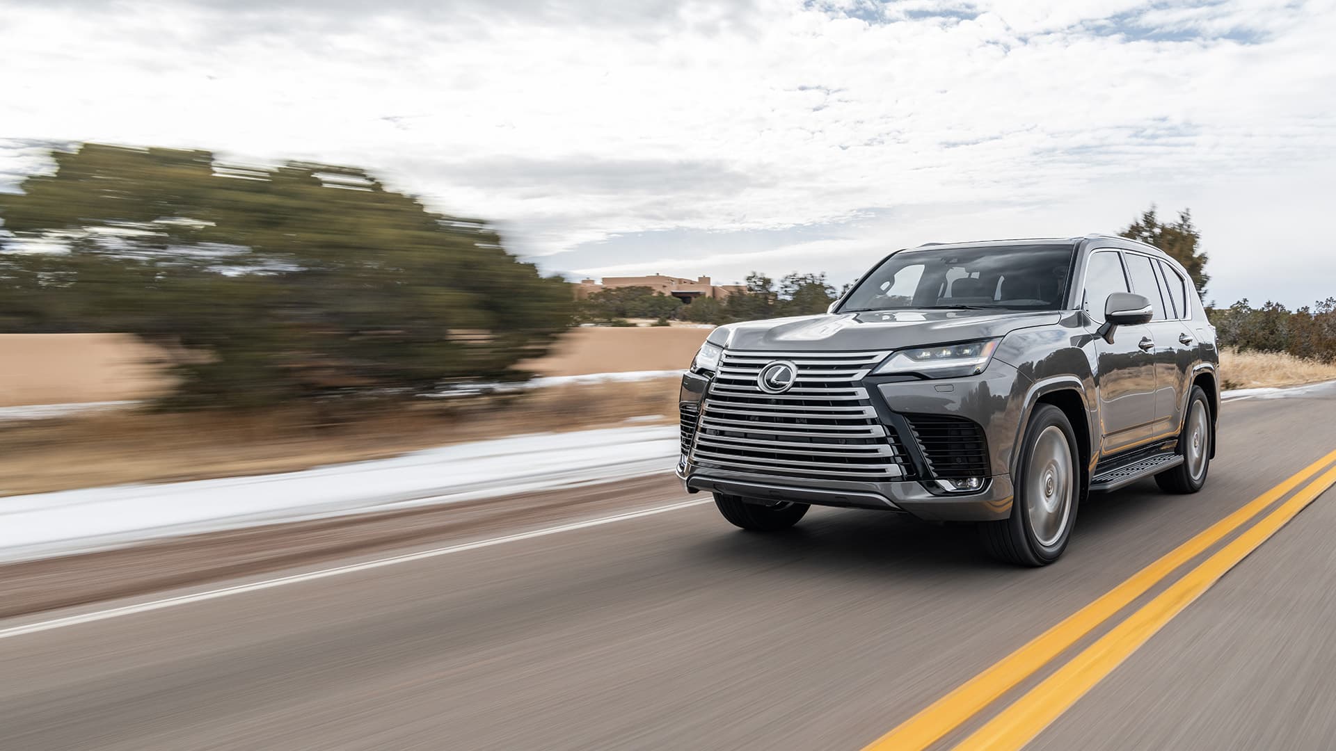 Silver Lexus LX being driven on a road next to a sandy terrain.